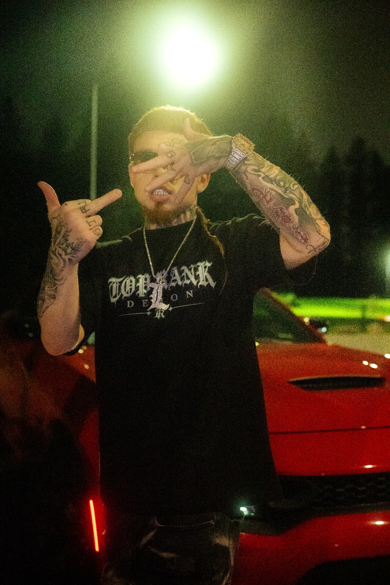 1TopRankDemon4 posing at night in the TOP RANK tee beside a red car